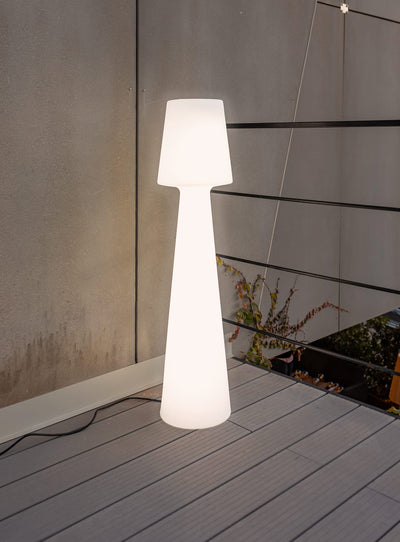 Lola 100 floor lamp in a living room, emitting warm white light from its plug-in version.